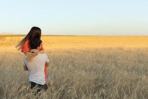 un joven hombre escogido arriba su mujer en su brazos y lleva su en puesta de sol en trigo campo. foto