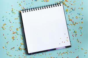 White open notebook on colorful background, festive, multicolored paper confetti. photo