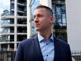 A Businessman pauses to reflect, dressed in business attire against an office building. The Businessman's thoughtful demeanor suggests deep deliberation. The Businessman stands as a symbol of resolve photo