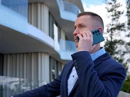 un empresario se involucra en un teléfono conversacion fuera de un oficina edificio, vestido en formal negocio atuendo. el del hombre de negocios profesional comportamiento es evidente como él discute importante asuntos. foto