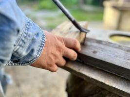 hombre toma un uña fuera un de madera tablero foto