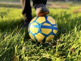 Close-up of a boy's foot in an old sneaker standing on a soccer ball. Green grass. photo