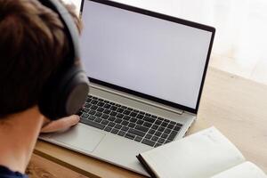 man in wireless headphones types on a laptop, notebook nearby, blank screen photo