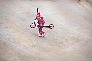 Active sporty child in overalls rides a pink scooter on an asphalt track photo