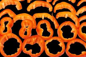 Red sweet ripe pepper cut into circles,slices on black photo