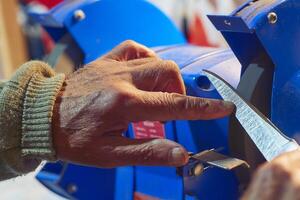 Sharpening a knife on a blue machine in the workshop photo