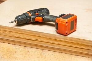 Electric drill,screwdriver on a plywood wooden surface with sawdust in workshop photo