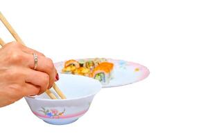 A woman's hand with chopsticks dips sushi into a bowl with soy sauce photo