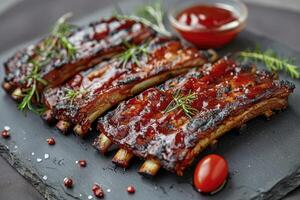 Tender and juicy BBQ pork ribs served with fresh herbs and tangy sauce on black slate board photo