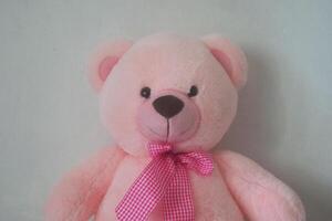 A cute pink teddy bear sits against a wall photo