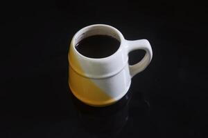 negro café en un blanco y amarillo taza en un negro cerámico mesa foto