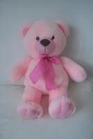 A cute pink teddy bear sits against a wall photo