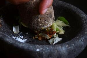 Someone is making chili sauce using a stone blender called Cobek photo