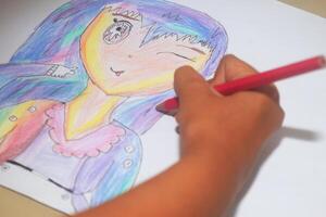 A small child is drawing and coloring an work made on paper photo