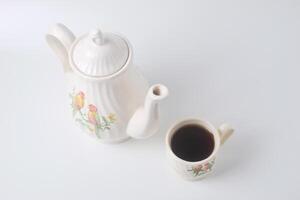 A cup of sweet tea with a ceramic teapot with a bird on a white background photo