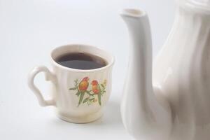 Close up photo of a cup of sweet tea and a white teapot with ceramic material