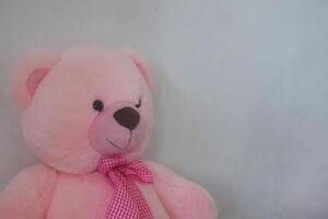 A cute pink teddy bear is leaning against a wall photo