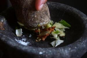Someone is making chili sauce using a stone blender called Cobek photo