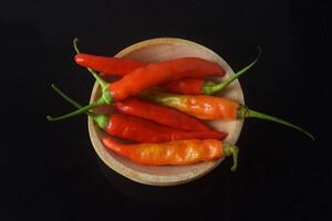 Some hot red chilies are sitting on a wooden plate photo