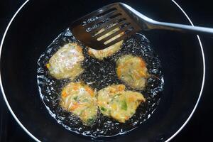 Someone is turning a dough of raw vegetables and wheat flour which is fried photo