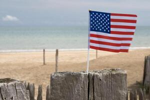 Utah Beach in Normandy, France. USA flag on wood sea fence. Sand, ocean and cloudy sky. photo