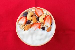 natural yogurt with homemade granola, strawberries and nuts in ceramic bowl on a red towel top view photo