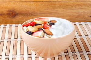 natural yogurt with homemade granola, strawberries and nuts in ceramic bowl on a table top view photo