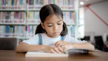 A young girl is sitting at a table in a library, reading a book photo