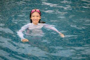 un joven niña es en el agua vistiendo un blanco camisa y rosado gafas de protección foto