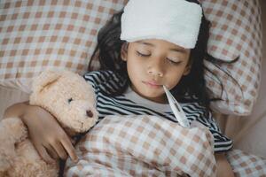 A young girl with a fever is lying in bed with a stuffed teddy bear photo