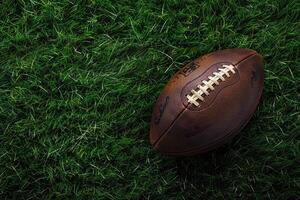 Brown American football ball on green artificial stadium turf background. photo