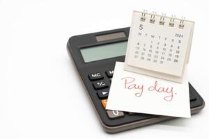 Hand writing text PAY DAY on May 2024 calendar with calculator in isolated background. Reminder concept of payment. copy space. photo