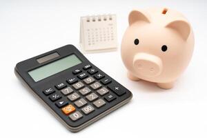 Piggy bank with calculator and calendar on white background, financial goal, money saving concept with copy space. Budget planning concept. photo