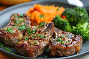 Roasted lamb chops with a side of mashed sweet potato and steamed vegetables. The steamed vegetables are a mix of broccoli and carrots. photo