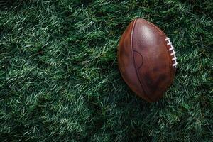 Brown American football ball on green artificial stadium turf background. photo