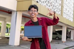 retrato de asiático Universidad estudiante utilizando ordenador portátil mirando a cámara. un hombre trabajando con un ordenador portátil computadora a instalaciones foto