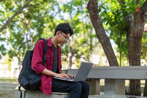 retrato de asiático Universidad estudiante utilizando ordenador portátil mirando a cámara. un hombre trabajando con un ordenador portátil computadora a instalaciones foto