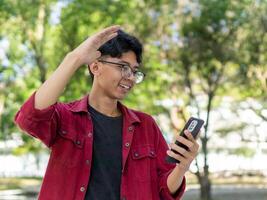 Asian man holding handphone and calling with friends waving hand making hello gesture. Man using smartphone for online conference call photo