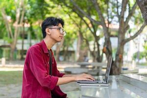 retrato de asiático Universidad estudiante utilizando ordenador portátil mirando a cámara. un hombre trabajando con un ordenador portátil computadora a instalaciones foto