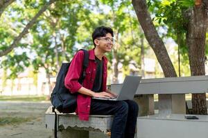 retrato de asiático Universidad estudiante utilizando ordenador portátil mirando a cámara. un hombre trabajando con un ordenador portátil computadora a instalaciones foto