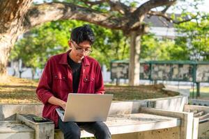 retrato de asiático Universidad estudiante utilizando ordenador portátil mirando a cámara. un hombre trabajando con un ordenador portátil computadora a instalaciones foto