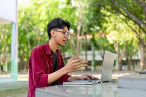 Young Asian man smiling while using laptop for working and conference meeting at the morning. Asian man having a call on laptop. Concept of remote and freelance photo