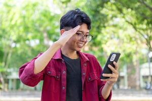 Asian man holding handphone and calling with friends waving hand making hello gesture. Man using smartphone for online conference call photo