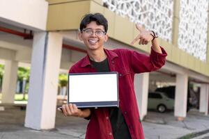 joven asiático hombre vistiendo rojo camisa sonriente y demostración blanco móvil teléfono pantalla para anuncio publicitario. concepto de personas estilo de vida. contento hombre participación blanco teléfono inteligente pantalla con borroso antecedentes. foto