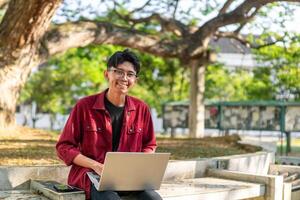 retrato de asiático Universidad estudiante utilizando ordenador portátil mirando a cámara. un hombre trabajando con un ordenador portátil computadora a instalaciones foto