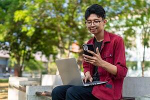 Young Asian man smiling while using laptop for working and conference meeting at the morning. Work from home. Young creative man looking at screen. photo