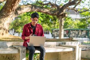 retrato de asiático Universidad estudiante utilizando ordenador portátil mirando a cámara. un hombre trabajando con un ordenador portátil computadora a instalaciones foto