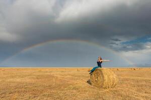 hermosa joven niña en un campo con Paja en un antecedentes de arco iris foto