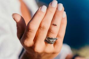 Ant walking by woman hand with a ring with feathers on her finger photo