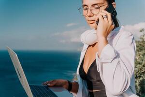 Woman sea laptop. Business woman, freelancer with laptop working over blue sea beach. Happy smiling girl relieves stress from work. Freelance, remote work on vacation, digital nomad, travel concept photo